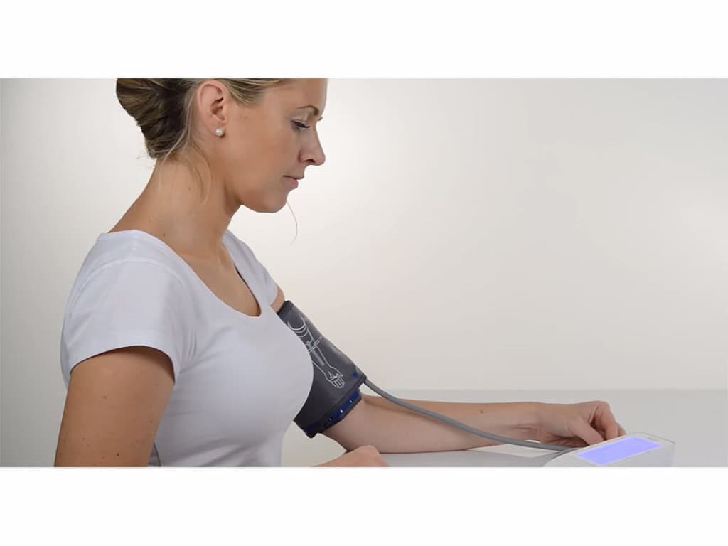 Vrouw meet haar bloeddruk aan tafel met de Beurer BM 49 bovenarm bloeddrukmeter en een manchet om haar arm