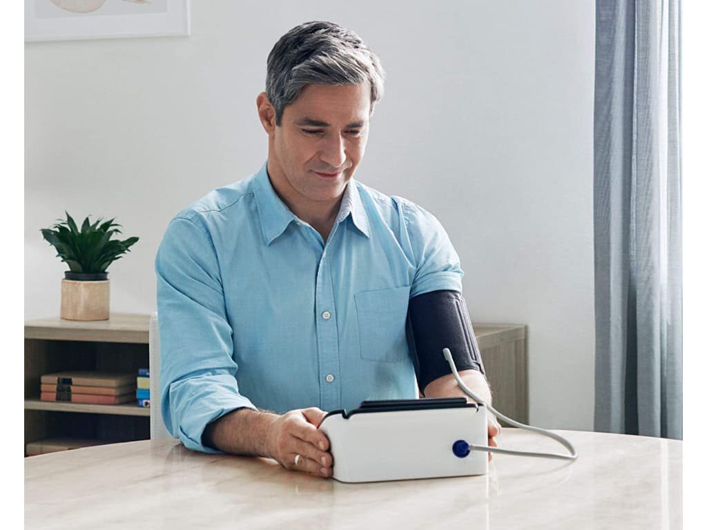 Man meet zijn bloeddruk en ECG met de Omron Complete vanaf de achterkant zichtbaar, met een smartphone op het apparaat waar hij naar kijkt