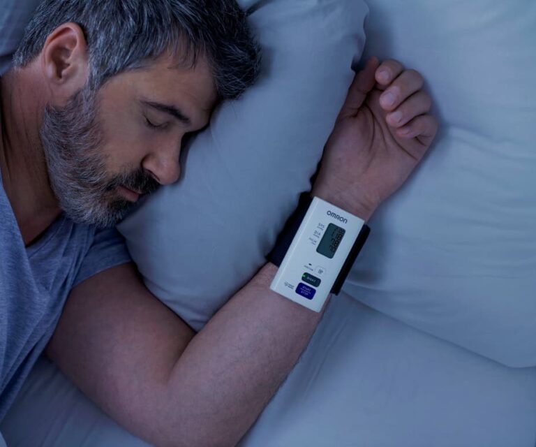 Man slaapt in bed met de Omron Nightview polsbloeddrukmeter om zijn pols