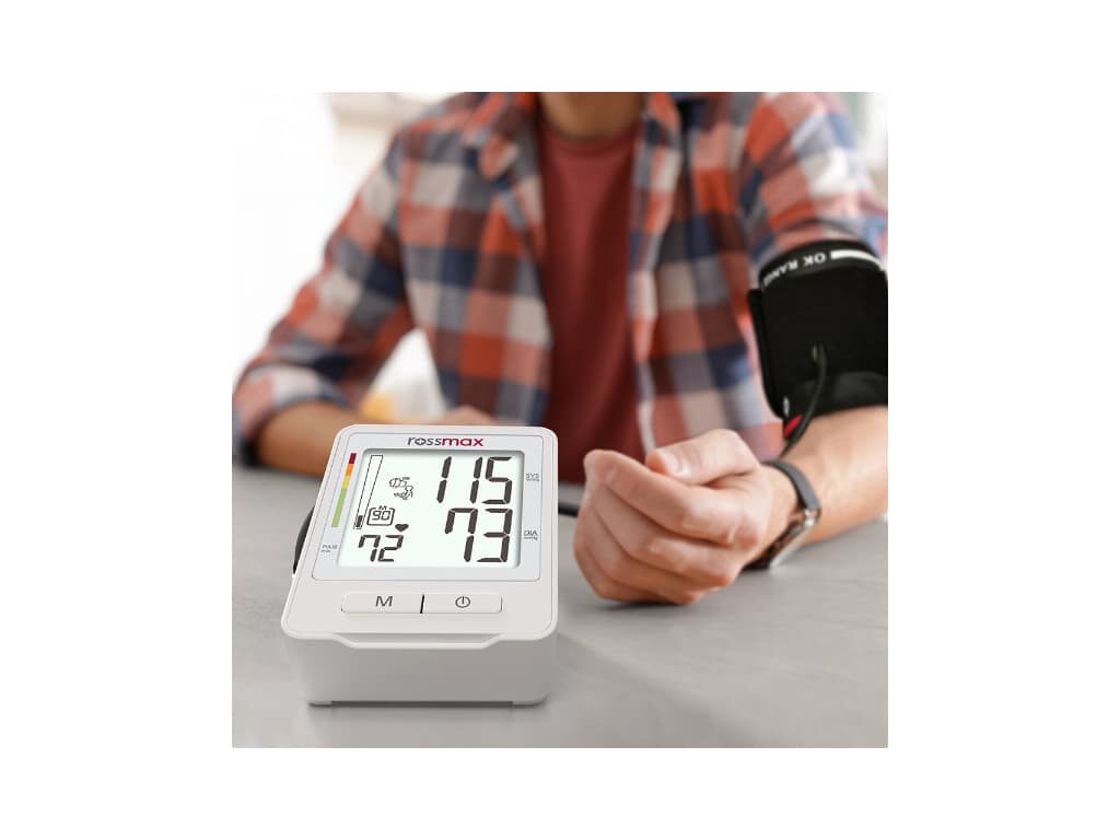 Rossmax Z1 bovenarm bloeddrukmeter op de voorgrond met aangesloten manchet om de arm van een persoon die op de achtergrond zijn bloeddruk meet