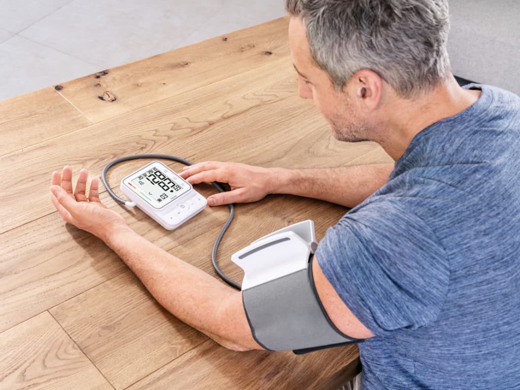 Man meet zijn bloeddruk aan tafel met de Beurer BM 51 easyClip bovenarm bloeddrukmeter en easyClip-manchet om de arm