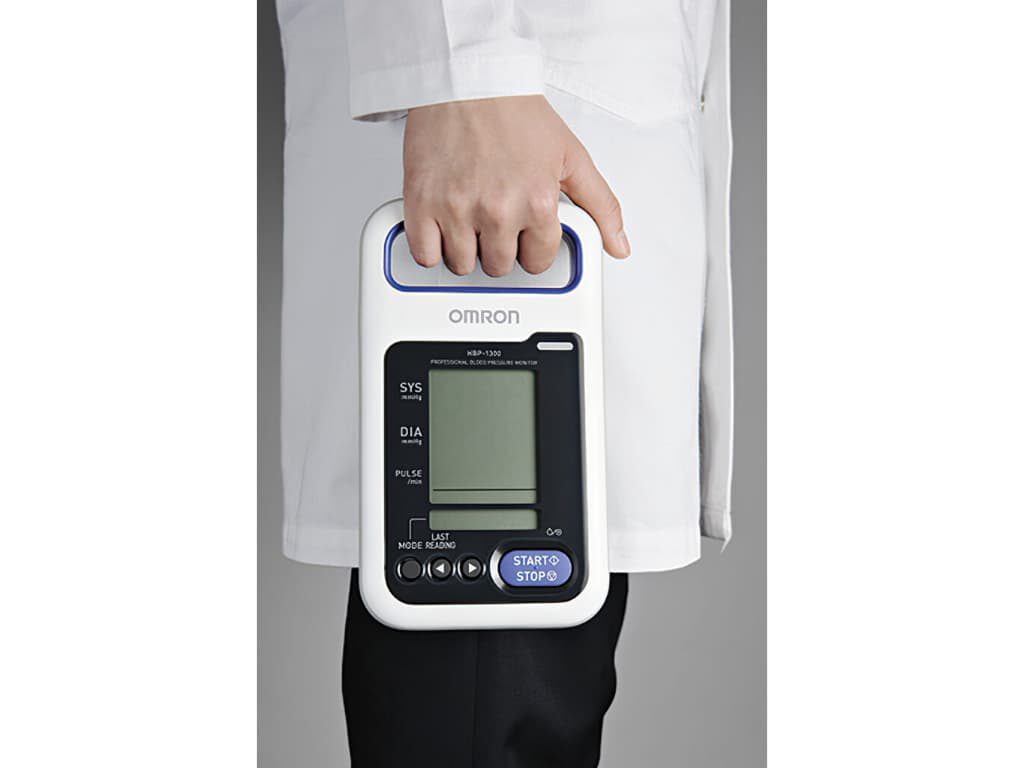 Persoon in witte jas houdt de Omron HBP-1320 professionele bloeddrukmeter vast aan het handvat