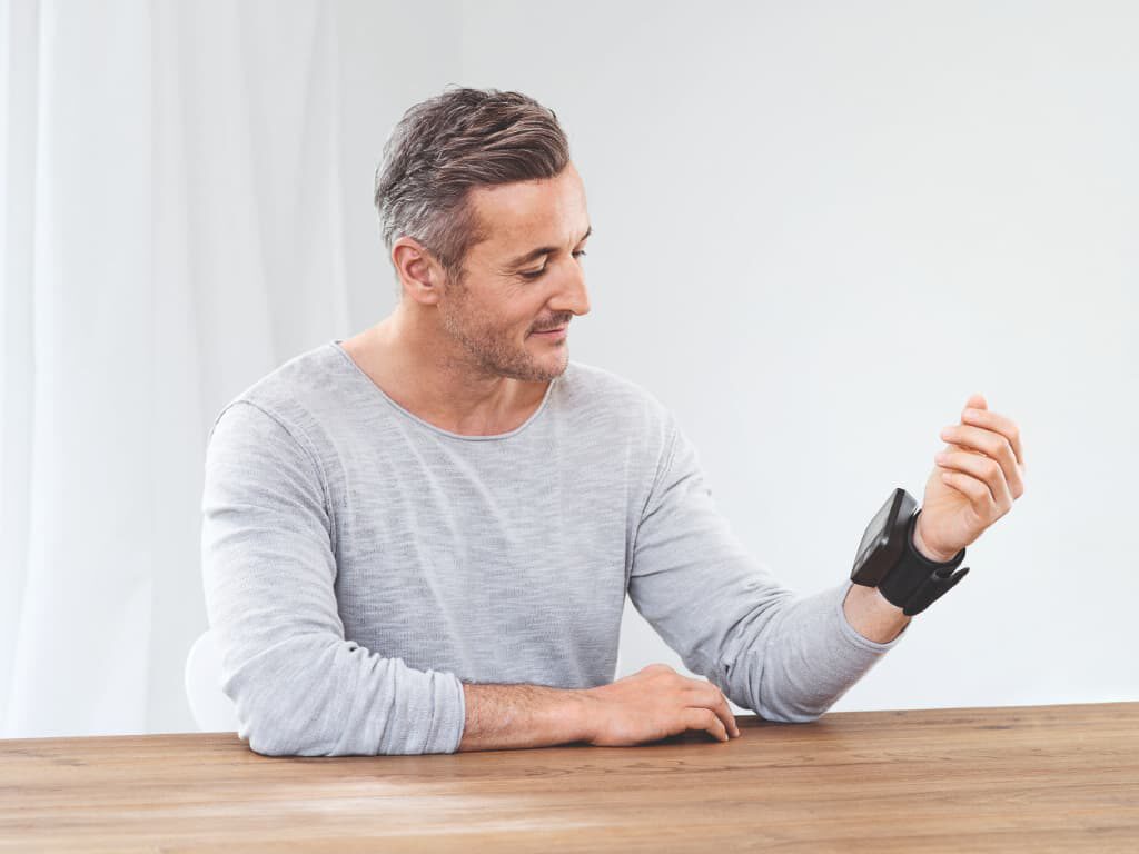Man zit aan tafel met de Beurer BC 54 polsbloeddrukmeter om zijn pols