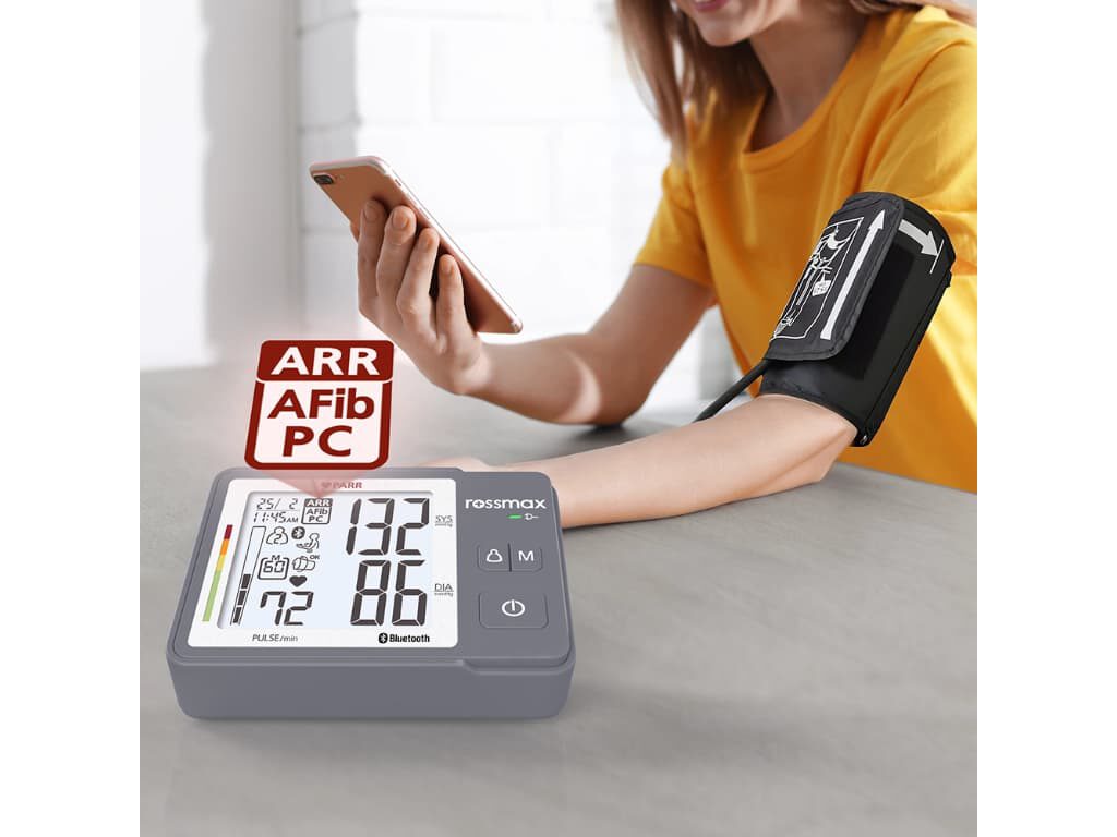 Rossmax Z5 bovenarm bloeddrukmeter op de voorgrond met icoon en de tekst “ARR AFib PC”, met op de achtergrond een vrouw die haar bloeddruk meet met manchet om de arm en een smartphone in de hand