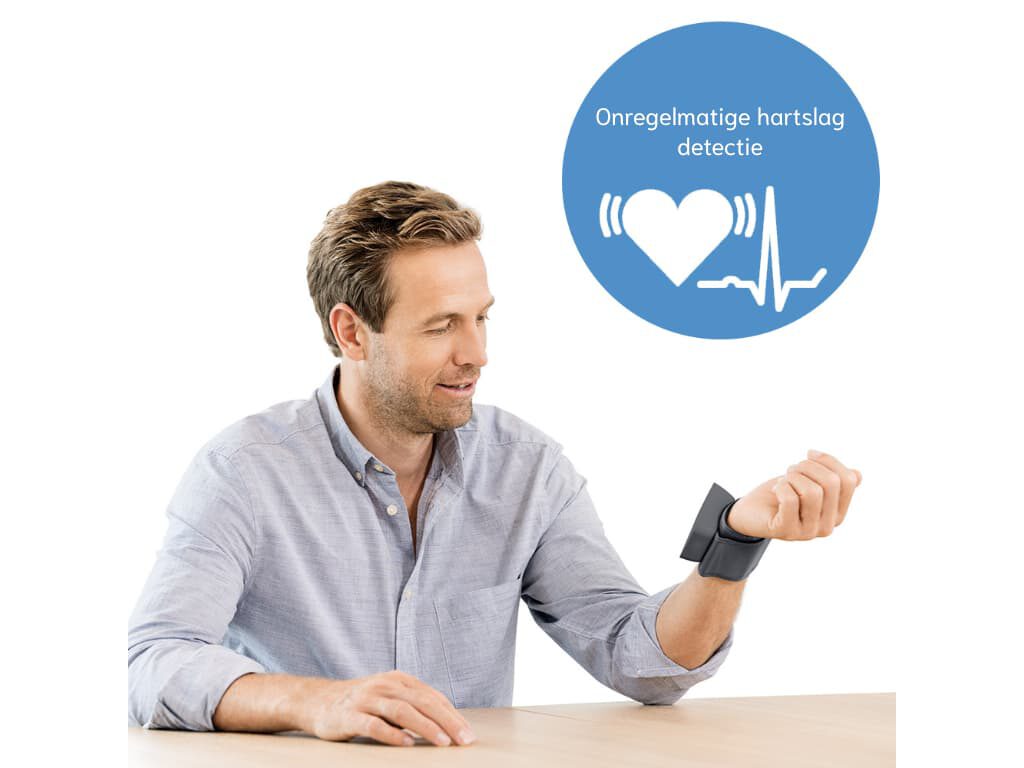 Man zit aan tafel met de Beurer BC 27 polsbloeddrukmeter om zijn pols, met een cirkel met harticoon en de tekst “Onregelmatige hartslag detectie” in beeld