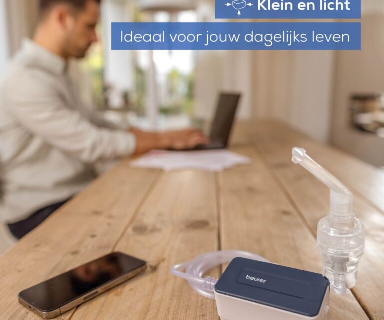 Beurer IH 15 vernevelaar en smartphone op tafel, man werkt op laptop op de achtergrond